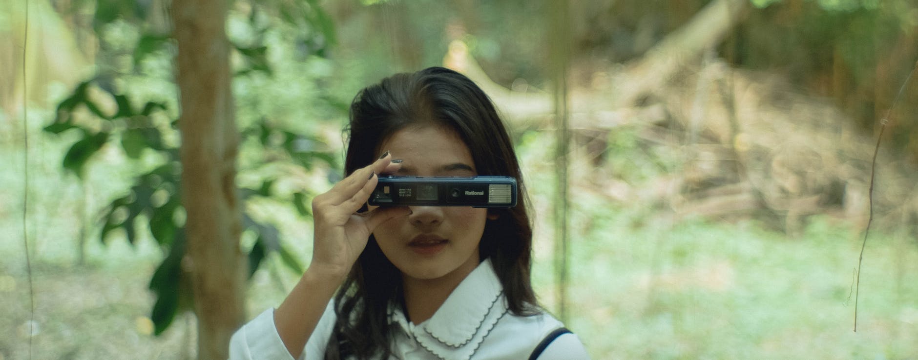 green image of a brunette girl wearing white shirt with collar holding a camera with flash